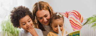 Woman sat in armchair with two small children, reading a storybook.